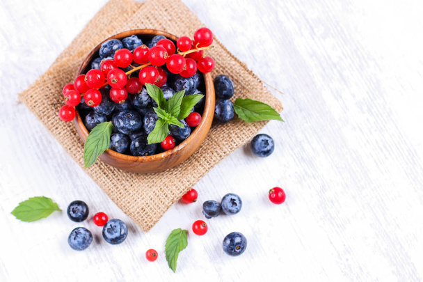 Fresh blueberries and red currants with mint leaves in a wooden bowl on burlap. Diet food, vegan berries - Foto, Bild
