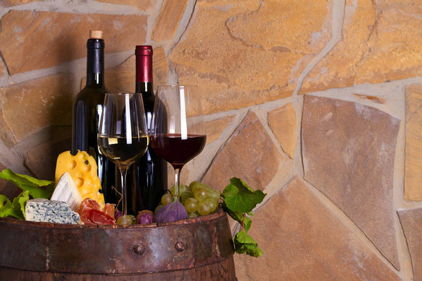 Rode en witte wijn met druiven op oude vat in wijnkelder. Glazen en flessen wijn met kaas, Jamon, vijgen en noten. Ruimte voor tekst, ruimte kopiëren - Foto, afbeelding