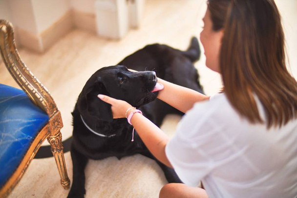 Young beautiful woman at home playing with black labrador dog - Photo, Image