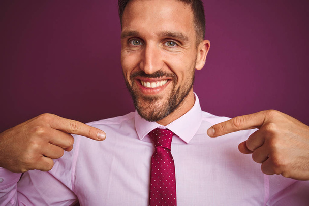 Közeli kép üzletember visel elegáns ing és a nyakkendő felett lila elszigetelt háttér néz magabiztos mosollyal az arcon, rámutatva önmagára ujjaival büszke és boldog. - Fotó, kép