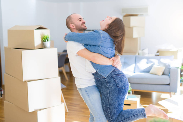Young couple hugging in love arround carboard boxes at new home, celebrating very happy moving to new apartment - Photo, image