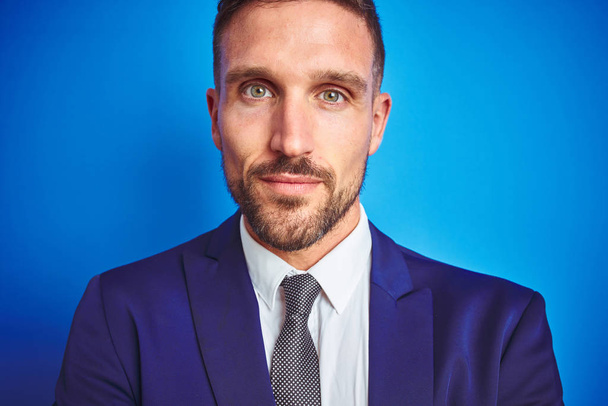 Close up picture of young handsome business man over blue isolated background Relaxed with serious expression on face. Simple and natural with crossed arms - Foto, imagen