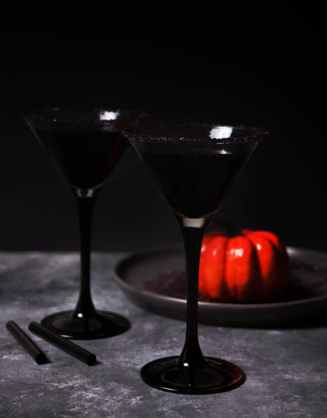 Two glasses with black cocktail, dried roses, pumpkin for Halloween party on the dark background - Valokuva, kuva