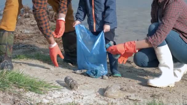 Planeten aus Plastik retten, junge Familienhelfer mit Kind in Gummihandschuhen sammeln Müll im Müllsack ein, während sie schmutzige Böschungen säubern - Filmmaterial, Video