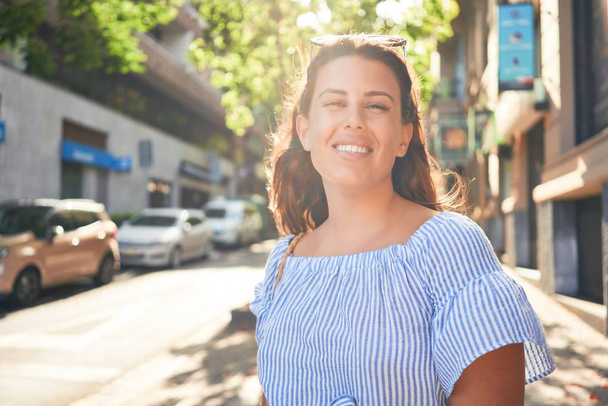 jonge mooie vrouw glimlachen gelukkig wandelen in de stad straten op een zonnige dag van de zomer - Foto, afbeelding