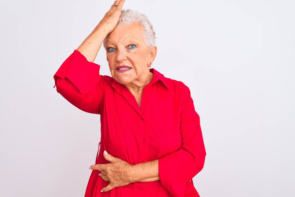 Senior grauhaarige Frau in rotem Hemd lässig vor isoliertem weißen Hintergrund stehend überrascht mit der Hand auf dem Kopf für Fehler, erinnere dich an Fehler. Vergessenes, schlechtes Gedächtnis. - Foto, Bild