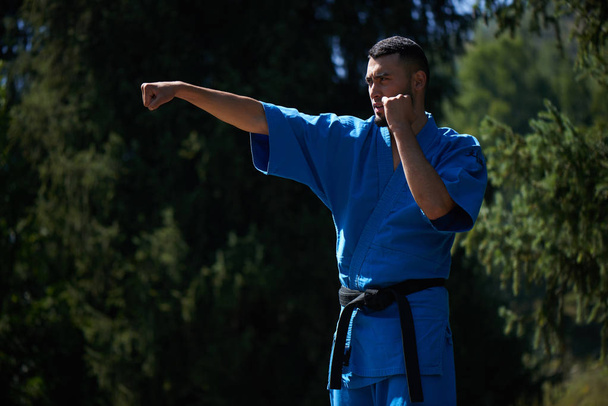 Asian Kazakh karate fighter is combat in blue kimono uniform on a summer beautiful nature landscape - Photo, Image