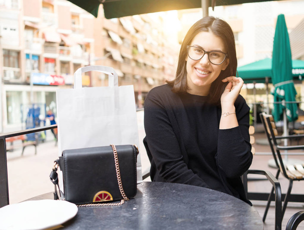 Красива молода жінка посміхається щасливо сидячи в кафе міста
 - Фото, зображення
