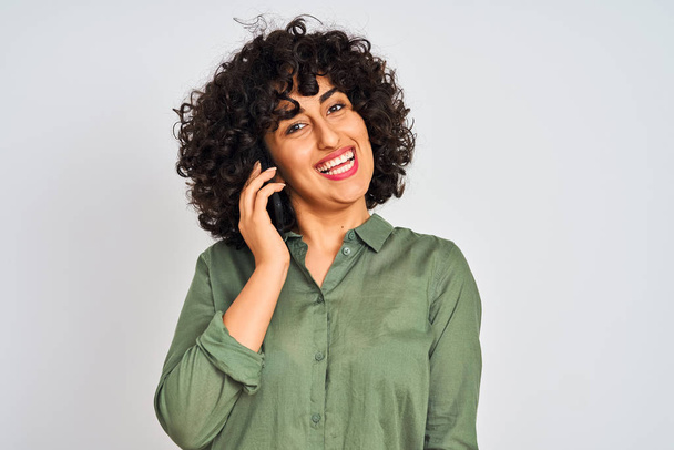 Young arab woman with curly hair talking on smartphone over isolated white background with a happy face standing and smiling with a confident smile showing teeth - Фото, зображення