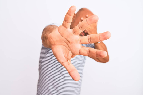 Middle age handsome man wearing striped navy t-shirt over isolated white background covering eyes with hands and doing stop gesture with sad and fear expression. Embarrassed and negative concept. - Foto, imagen