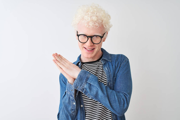 Молодой белокурый альбинос в джинсовой рубашке и очках на изолированном белом фоне хлопает и аплодирует счастливым и радостным, улыбающимся гордым рукам вместе
 - Фото, изображение