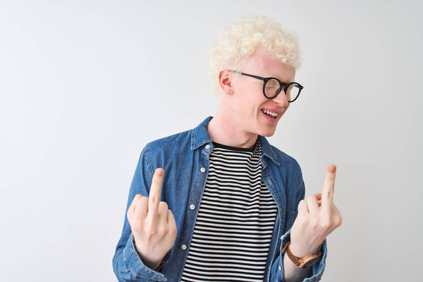 Mladý albín blonďatý muž v džínové košili a brýlích na izolovaném bílém pozadí Ukazující prostředníček dělá hovno výraz, provokace a hrubý postoj. Nadšený křik - Fotografie, Obrázek