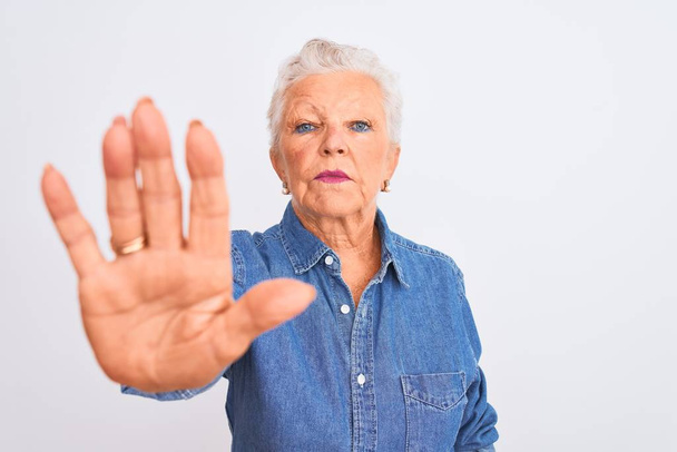 Senior grey-haired woman wearing casual denim shirt standing over isolated white background with open hand doing stop sign with serious and confident expression, defense gesture - Photo, Image
