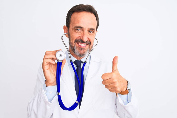 Muž středního věku pomocí stetoskopu stojí nad izolovaným bílým pozadím šťastný s velkým úsměvem dělá ok znamení, palec nahoru s prsty, vynikající znamení - Fotografie, Obrázek