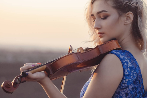 portrait of a beautiful young woman with a violin under her chin at sunset, girl playing a musical instrument on nature, concept music and hobbies - Foto, afbeelding