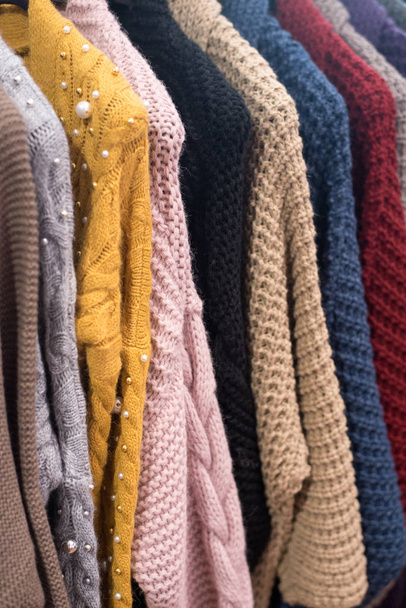 knitted sweaters and cardigans hang on a floor hanger. Colored big knitwear in the wardrobe. - Photo, Image