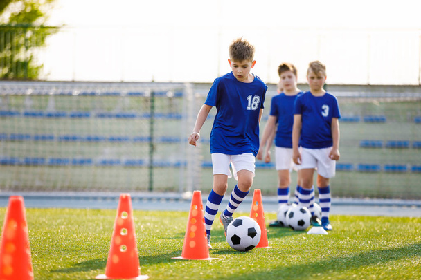 Ποδοσφαιρική προπόνηση με τρυπάνι από κώνο. Νεαρά Αγόρια του Σχολείου Junior Soccer Team Εξάσκηση στο γρασίδι. Παιδιά βελτίωση ποδοσφαιρικών δεξιοτήτων - Φωτογραφία, εικόνα
