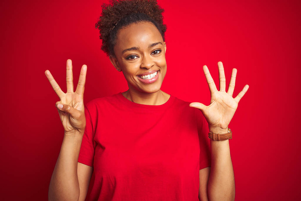 Mladá krásná africká americká žena s afro vlasy přes izolované červené pozadí ukazující a ukazující nahoru s prsty číslo osm při úsměvu sebevědomě a šťastně. - Fotografie, Obrázek