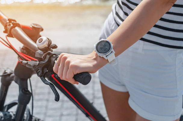 Woman's hand on bicycle handlebar, white smart watch on wrist - Foto, immagini