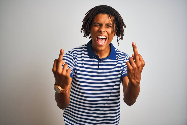 Afro man with dreadlocks wearing striped blue polo standing over isolated white background Showing middle finger doing fuck you bad expression, provocation and rude attitude. Screaming excited - Foto, afbeelding