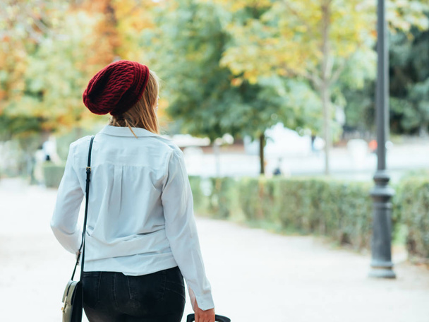 Caucasian girl with red beret and white shirt, walks with her suitcase through the park of Buen Retiro in Madrid, Spain. - Fotó, kép