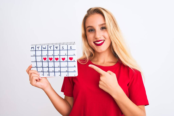 junge schöne Frau mit Zeitrahmen Kalender steht über isolierten weißen Hintergrund sehr glücklich zeigt mit Hand und Finger - Foto, Bild