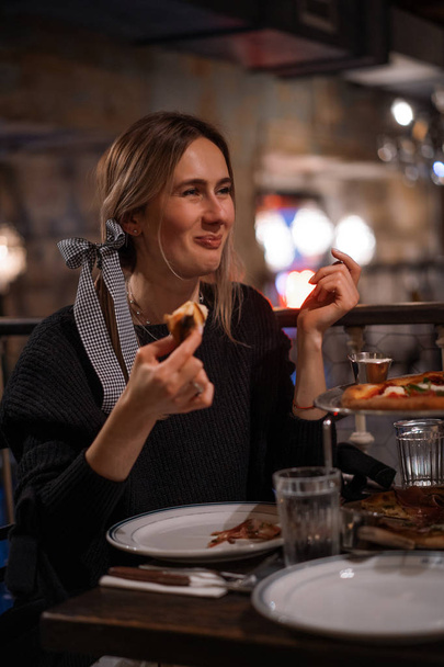 Young beautiful woman in a pizzeria eats juicy pizza. - Фото, зображення