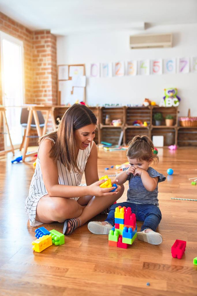 Jeune belle enseignante et tout-petit jouant avec des blocs de construction jouet à la maternelle
 - Photo, image
