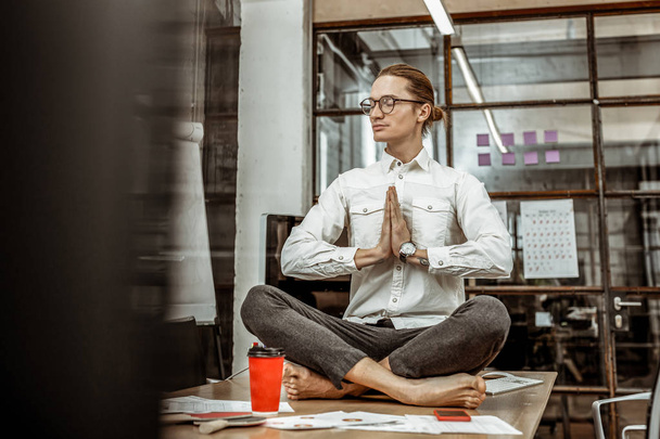 Cheerful male person doing yoga at his workplace - Foto, imagen