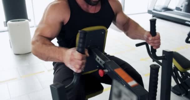 Silný muž cvičící svaly na sportovním simulátoru ve sportovním klubu. Sportovec cvičí na fitness stroji v moderní tělocvičně - Záběry, video