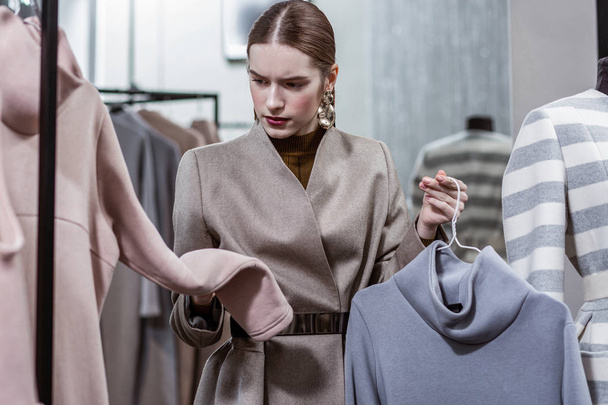 Concentrated woman looking closely at clothes in shop - 写真・画像