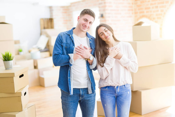 Beautiful young couple moving to a new house smiling with hands on chest with closed eyes and grateful gesture on face. Health concept. - Φωτογραφία, εικόνα