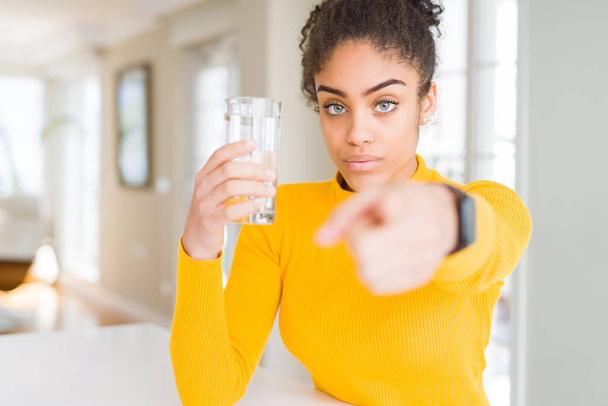 Jovem afro-americana bebendo um copo de água doce apontando com o dedo para a câmera e para você, sinal de mão, gesto positivo e confiante da frente
 - Foto, Imagem