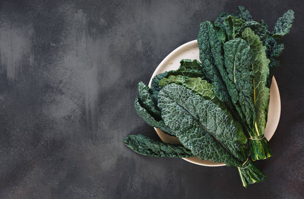 Fresh  Tuscan kale leaves on a white plate and on rustic dark background. Top view, blank space - Valokuva, kuva
