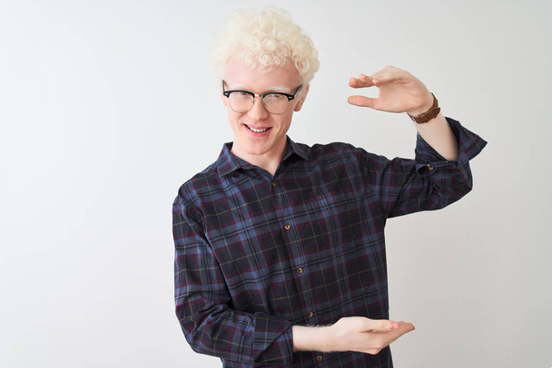 Jonge albino blonde man draagt casual shirt en bril over geïsoleerde witte achtergrond gebaren met handen tonen grote en grote maat teken, maat symbool. Lachend kijkend naar de camera. Meetconcept. - Foto, afbeelding
