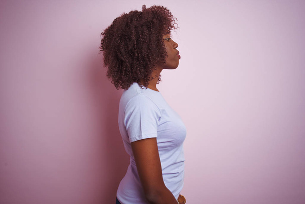 Young african afro woman wearing t-shirt standing over isolated pink background looking to side, relax profile pose with natural face with confident smile. - Fotografie, Obrázek