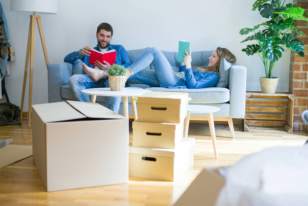junges Paar entspannt auf dem Sofa, liest ein Buch und macht eine Pause für den Umzug in ein neues Haus - Foto, Bild