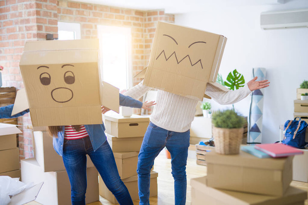 Couple fou portant des boîtes avec des visages drôles au-dessus de la tête, s'amusant heureux de déménager dans une nouvelle maison
 - Photo, image