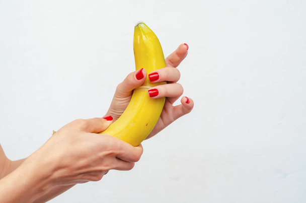 Female hands pull a condom on a yellow banana. Demonstration - Zdjęcie, obraz