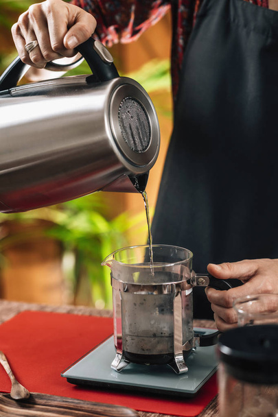 Französische Presse Kaffee. Barista gießt kochendes Wasser aus Wasserkocher in französischen Presskopf und wiegt es vor dem Brauen auf einer Waage. - Foto, Bild