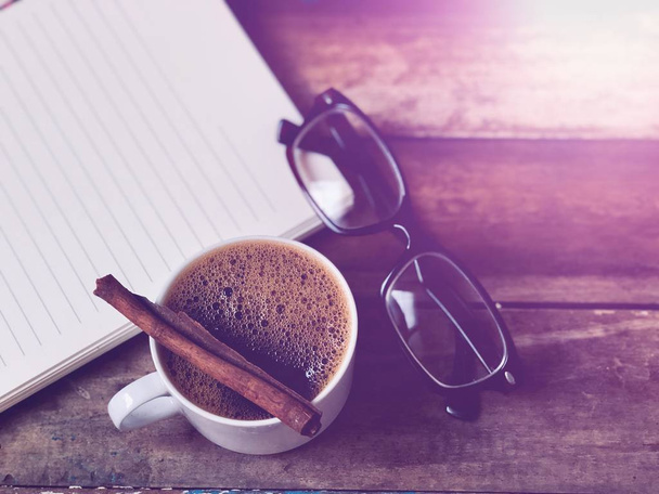 Eyeglasses on empty book,White mugs has Cappuccino coffee on wood table top,rustic still life,soft dark tone,dimly light,with lens flare,free space for your text. Concept of Relaxation in Coffee time - Fotoğraf, Görsel