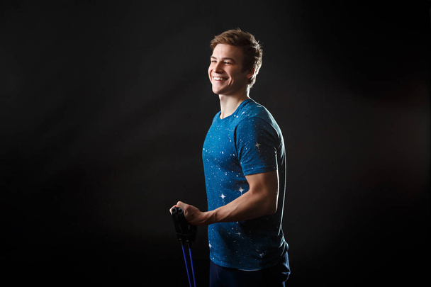 A male in blue t-shirt standing and smiling with fitness equipment in his hand - Foto, imagen