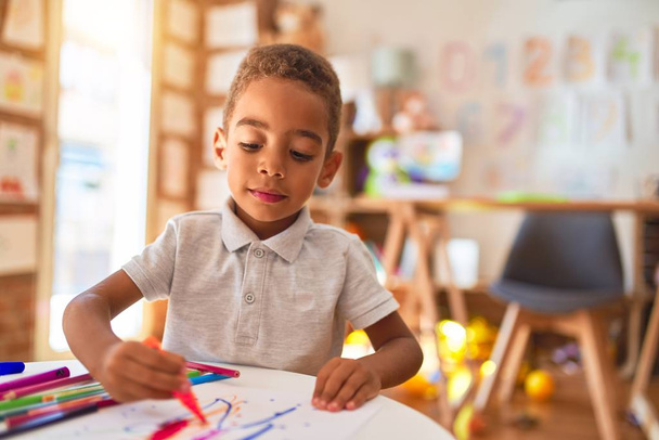 Hermoso dibujo de niño afroamericano usando papel y rotulador sonriendo en el jardín de infantes
 - Foto, Imagen