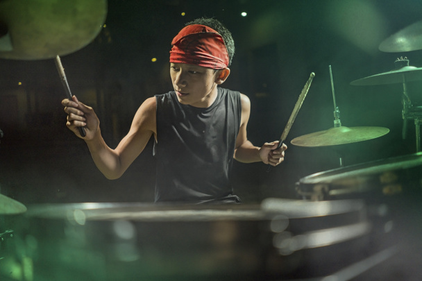 jonge jongen als rock band drummer. Knappe en koele Aziatische Amerikaanse tiener in hoofdband spelen Drum Kit uitvoeren nacht muziek show als hobby - Foto, afbeelding