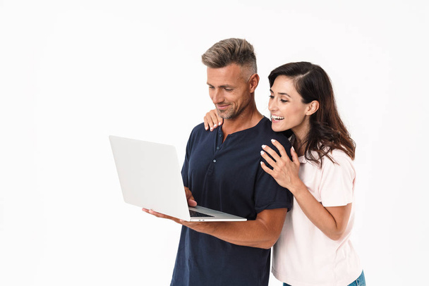 Cheery positive adult loving couple isolated over white wall background using laptop computer. - Fotó, kép