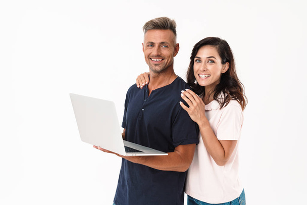 Cheery positive adult loving couple isolated over white wall background using laptop computer. - 写真・画像