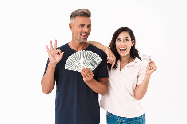 Surprised adult loving couple isolated over white wall background holding money and credit card. - Photo, image