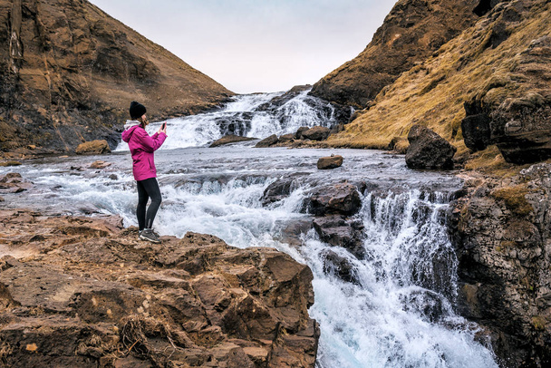 девушка фотографирует водопад на телефон - Фото, изображение