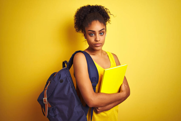 Amerikaanse student vrouw dragen rugzak met notebook over geïsoleerde gele achtergrond met een zelfverzekerde uitdrukking op slimme gezicht denken serieus - Foto, afbeelding