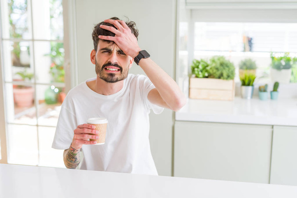 Young man drinking a coffee in a paper cup in the morning stressed with hand on head, shocked with shame and surprise face, angry and frustrated. Fear and upset for mistake. - Fotografie, Obrázek